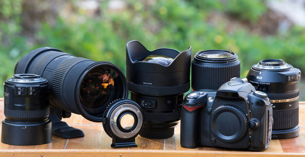 Photographe dans son bureau examinant attentivement plusieurs objectifs disposés sur son bureau pour comparer et choisir son équipement