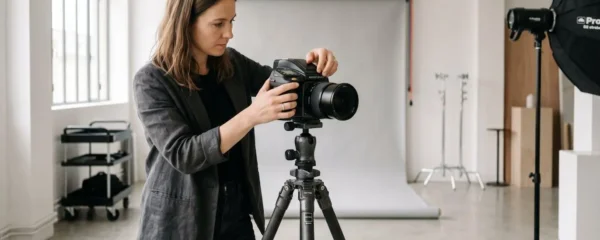 Photographe professionnel ajustant les réglages d'un appareil photo haut de gamme monté sur trépied dans un studio photo moderne avec équipement d'éclairage en arrière-plan